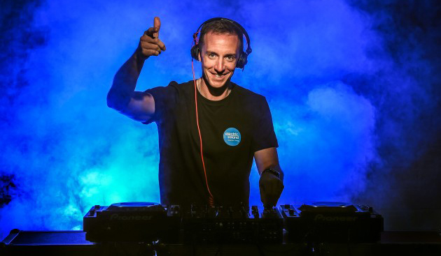 Bald DJ behind DJ decks wearing headphones